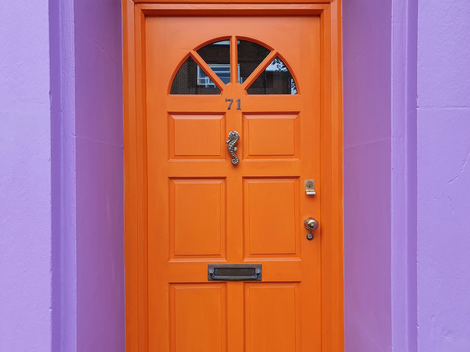 A bright orange panelled front door in a painted surround
