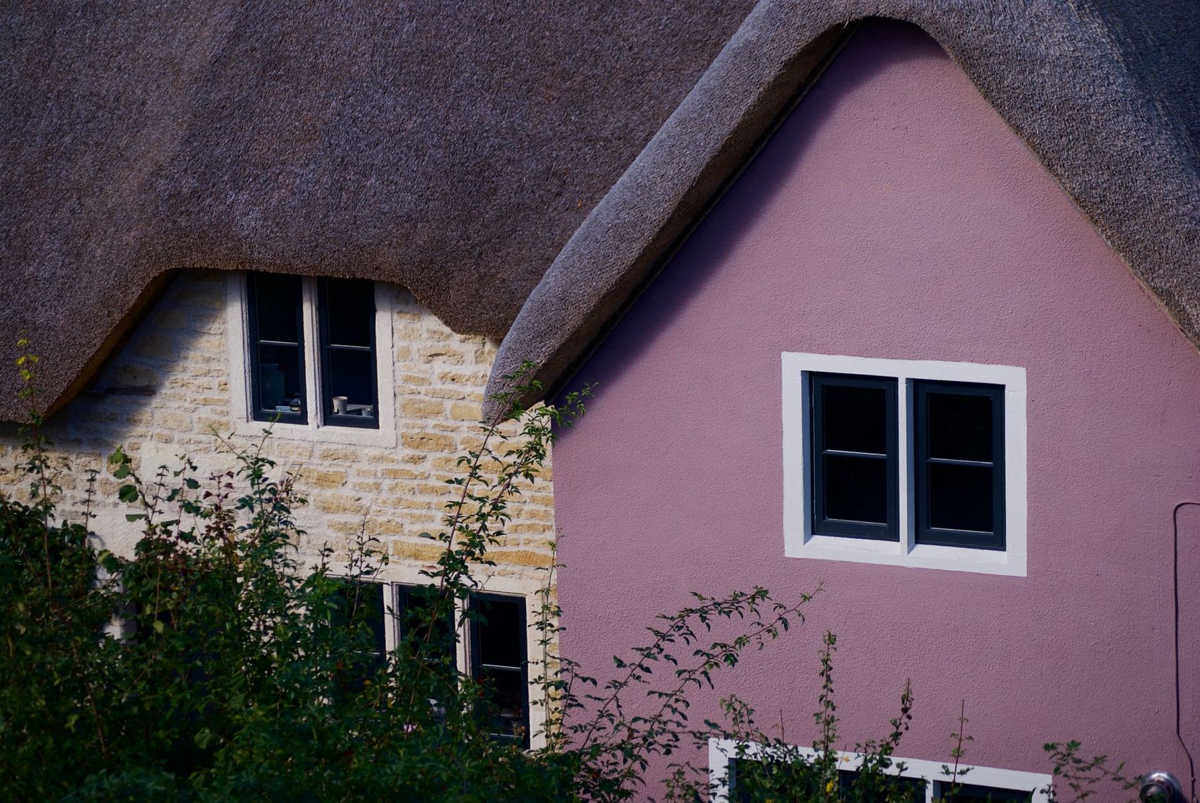 A pink-washed thatched cottage with white casement windows