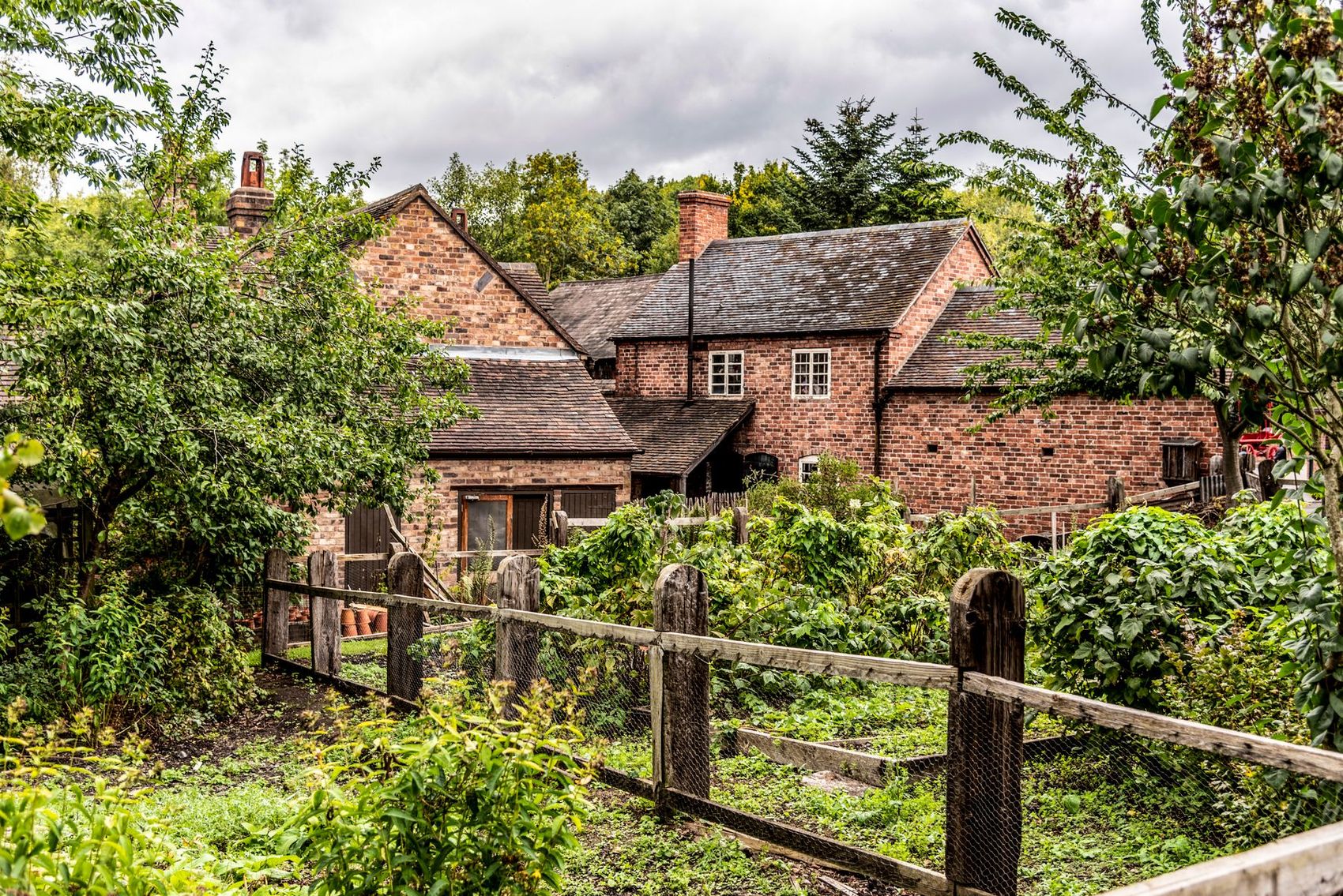 A brick English farmhouse behind a garden fence in summer
