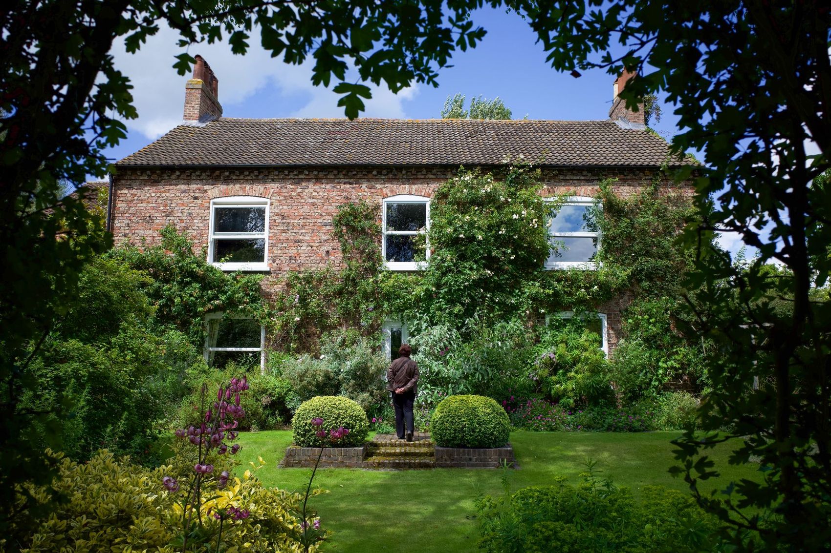 A brick English house behind a long summer garden