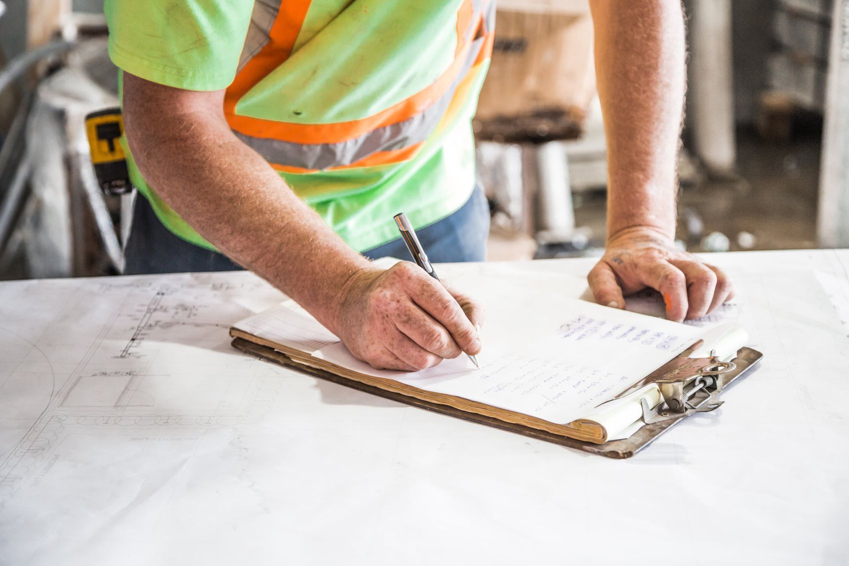 A surveyor recording measurements on a clipboard over the drawings